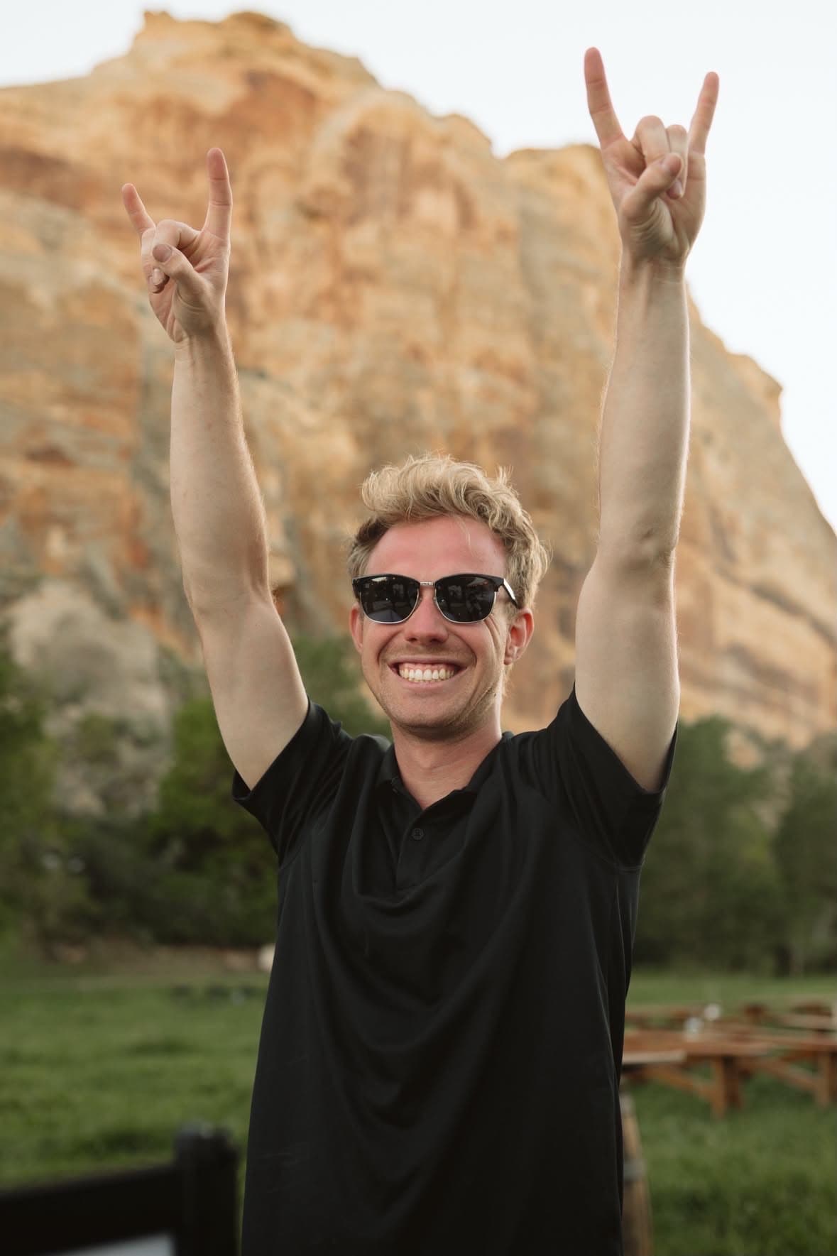 DJ Christian smiling with both hands raised in front of red rock cliffs
