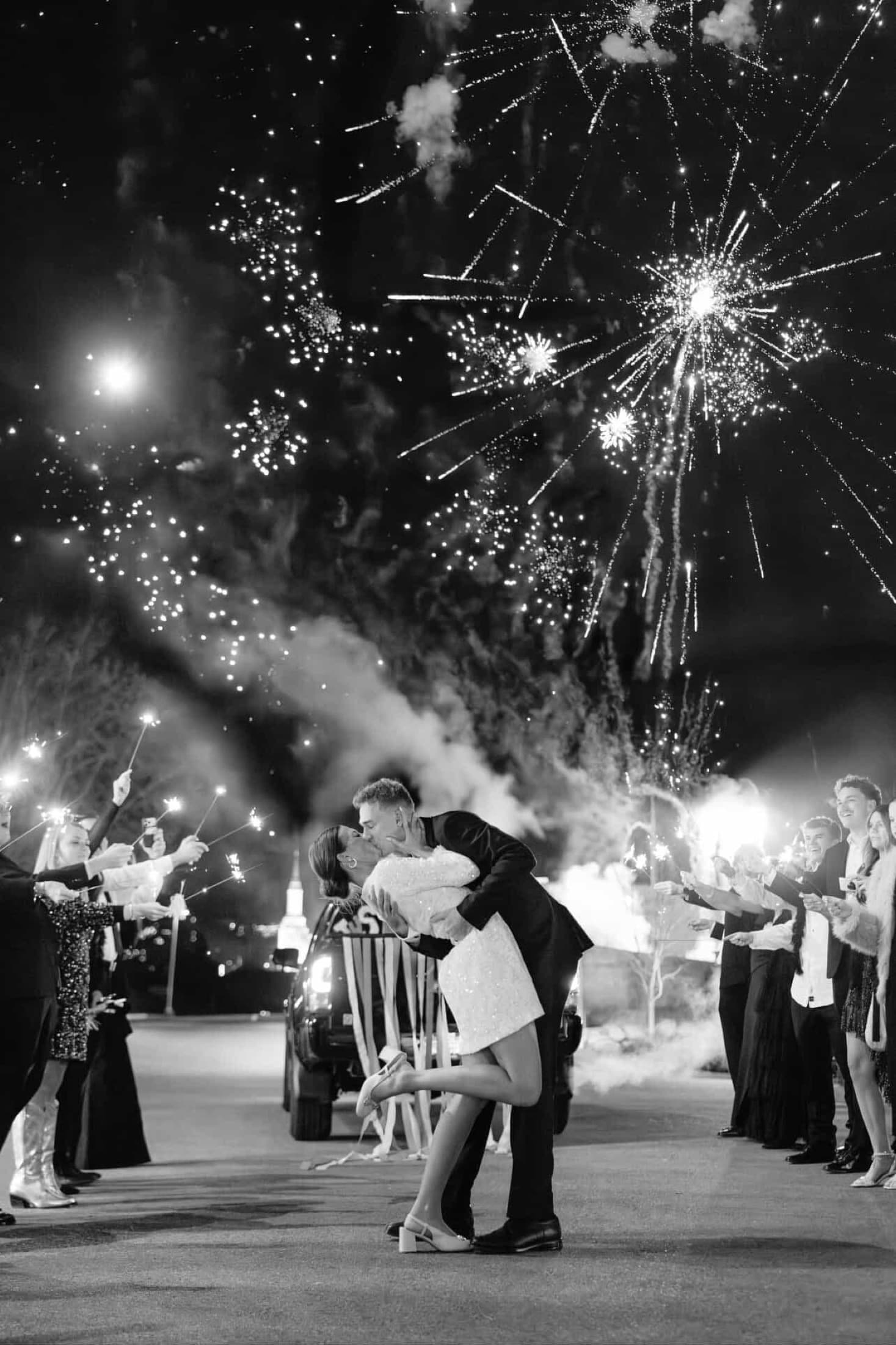 Newlyweds kissing beneath fireworks during a black-and-white wedding send-off