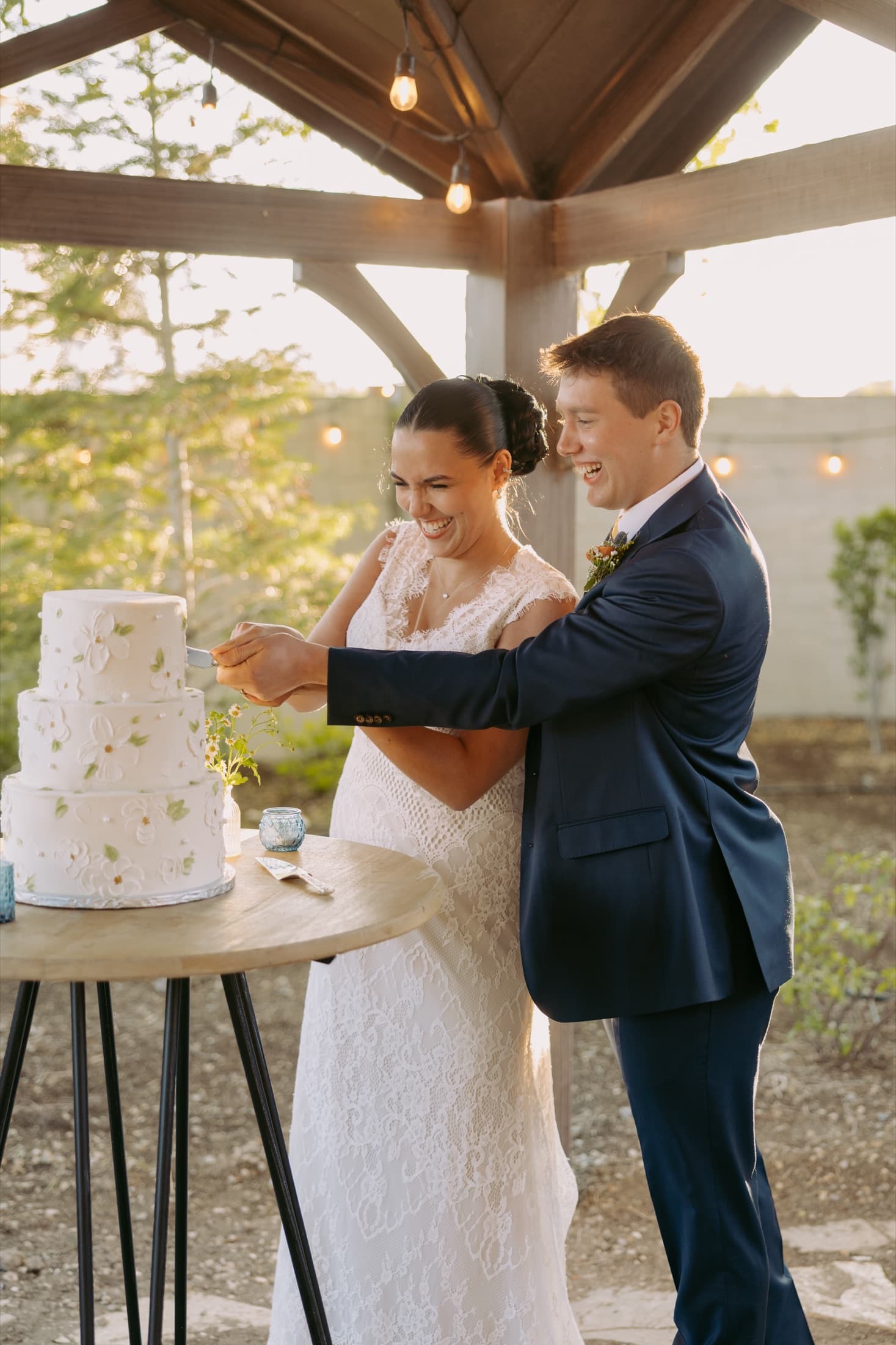Newlyweds laughing together as they cut their wedding cake at golden hour