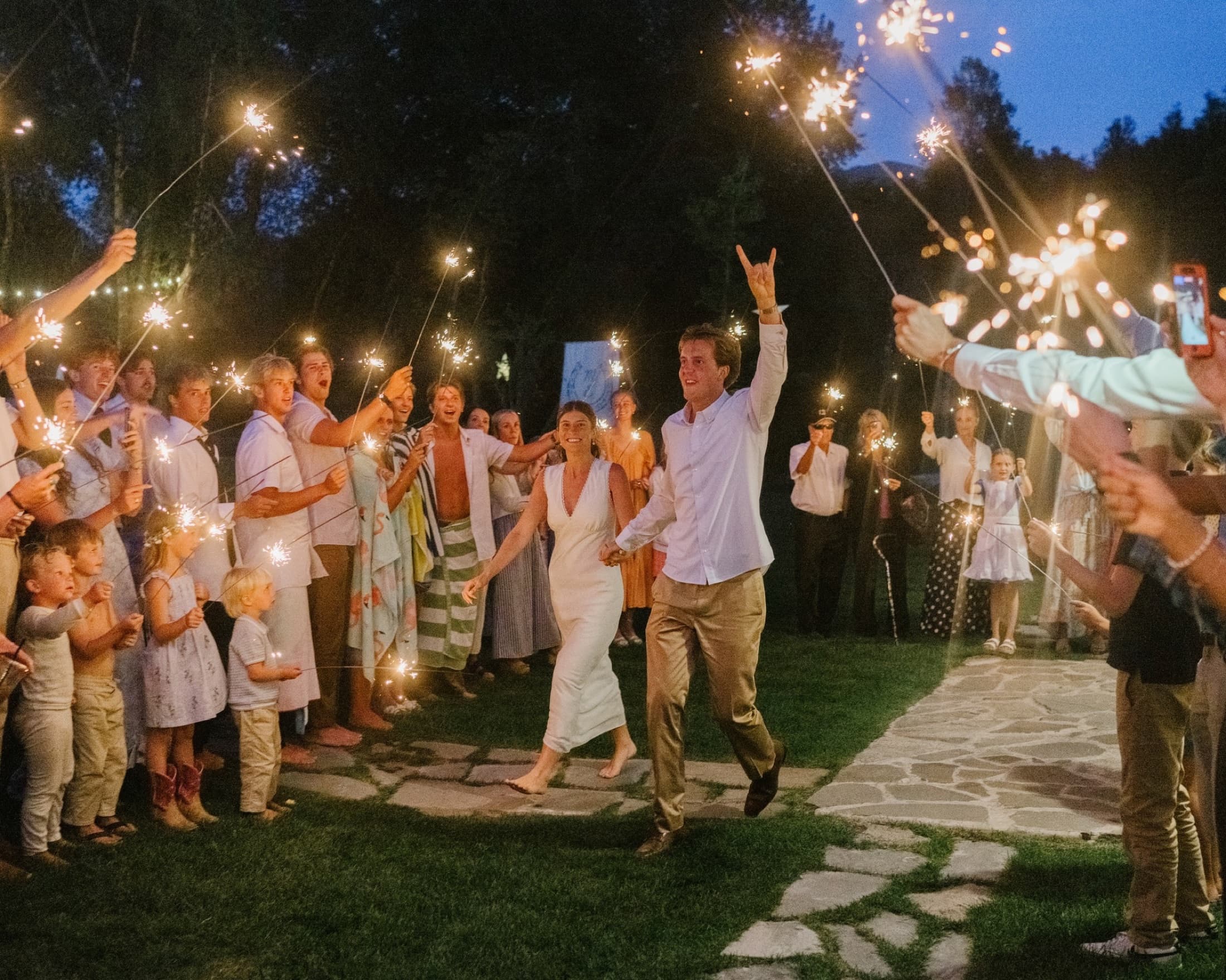 Newlyweds celebrating with guests holding sparklers after dark